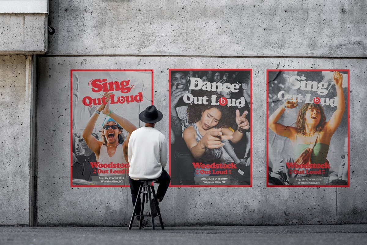 Three Woodstock Out Loud posters wheatpasted on a concrete wall, with a seated figure for scale